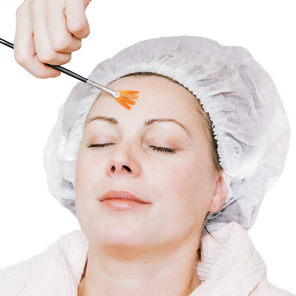 Врач наносит средство для пилинга на кожу лица пациента